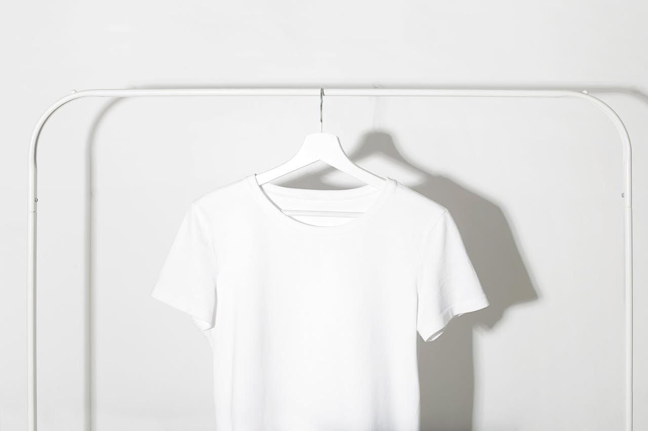 Plain white t-shirt on a hanger against a minimalist white backdrop with shadows.